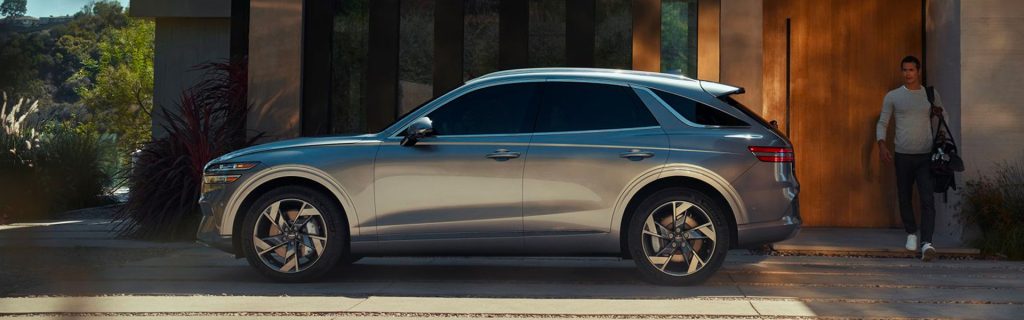 A Genesis luxury SUV parked outside a modern home, with a person walking toward it.