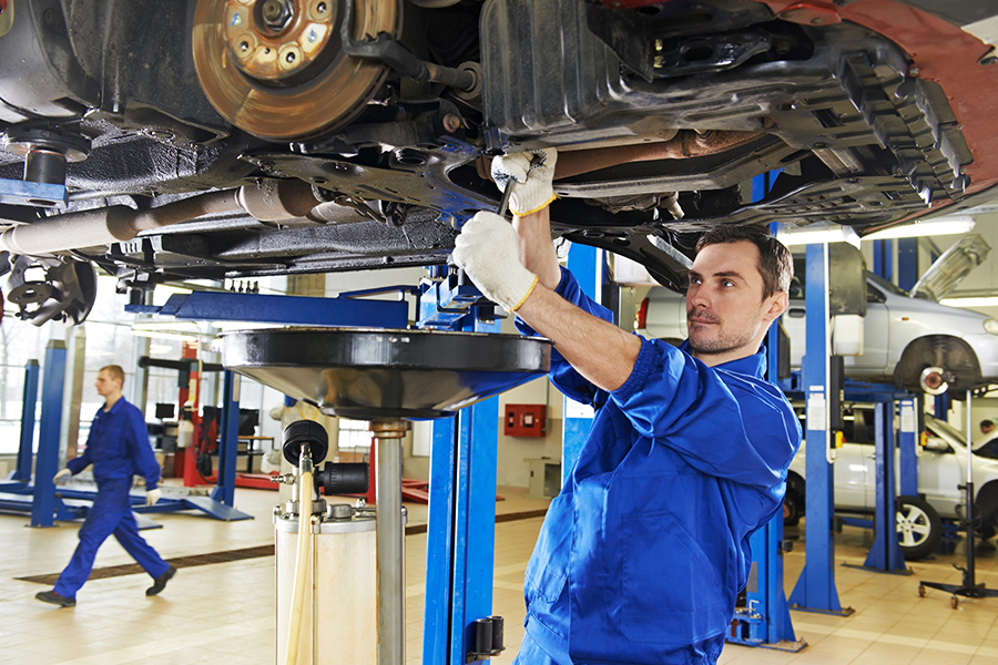 A mechanic working under a car in a service shop, performing maintenance or repairs.