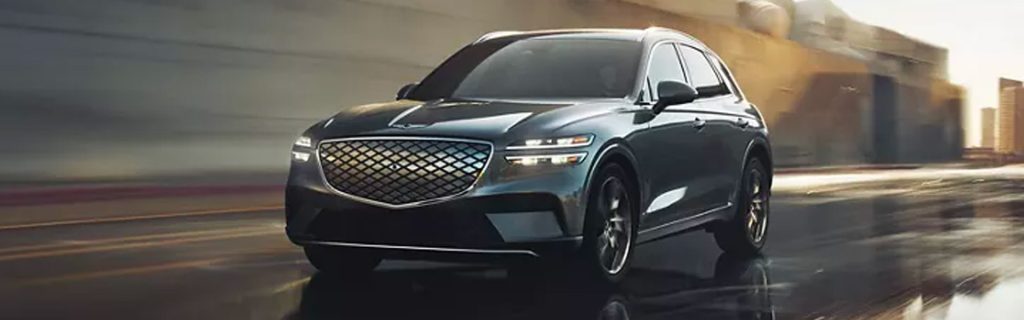 Genesis GV70 luxury SUV driving through a city street with motion blur and modern buildings in the background.