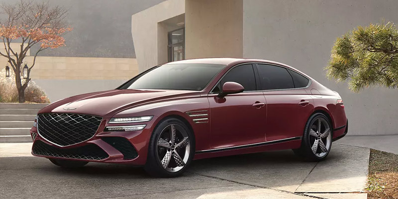 Red 2026 Genesis G80 luxury sedan parked outside a modern home, showcasing sleek design, signature grille, and premium styling.
