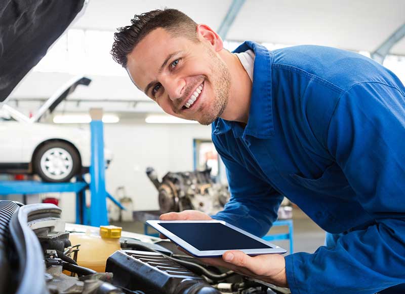 A technician examining the car while holding a tablet, appearing focused on the device and the vehicle.