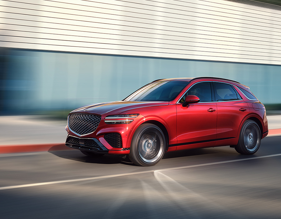 Red Genesis SUV driving at speed on a city street with a modern building backdrop, showcasing its sleek design and sporty stance.