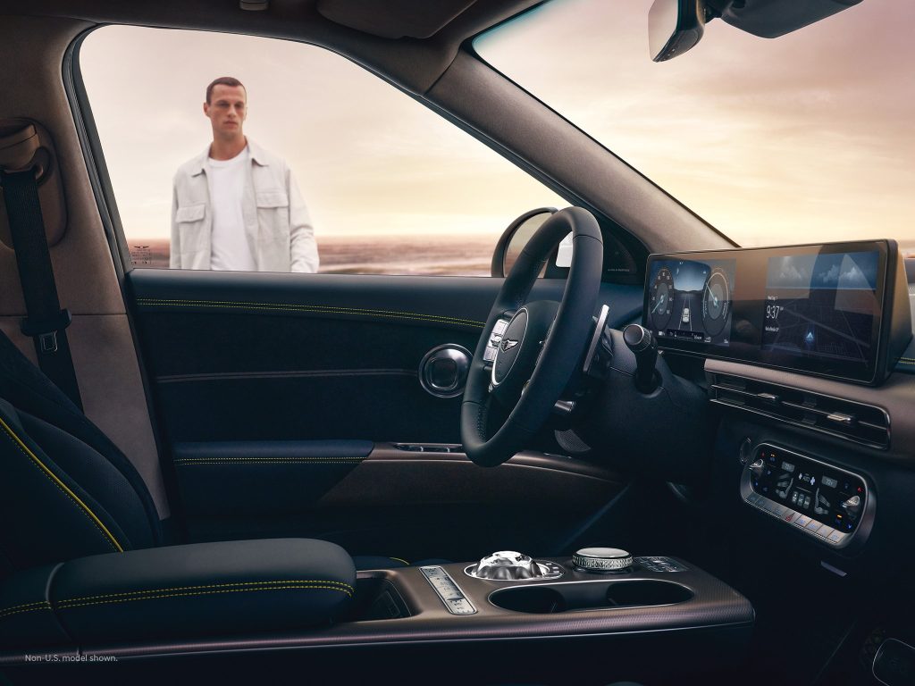 A man stands outside a Genesis car, gazing into the driver's seat, with the car's luxury interior clearly visible from the open door.