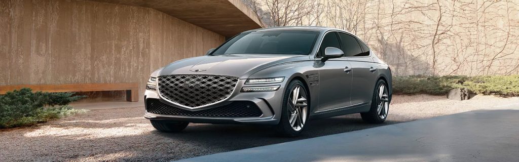 A sleek silver Genesis G80 parked in a driveway, showcasing a modern design with an intricate grille and stylish wheels.
