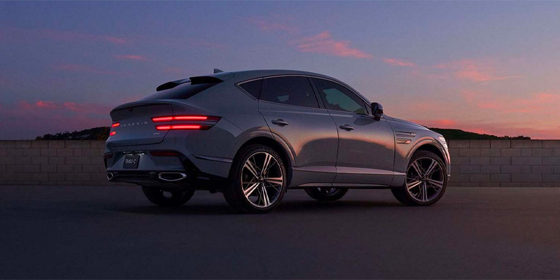 A silver Genesis GV80 Coupe parked against a sunset backdrop, showcasing its sleek design and modern features.