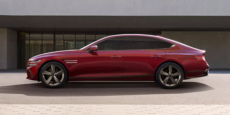 A sleek red Genesis G80 Luxury Sedan parked on a modern urban street.