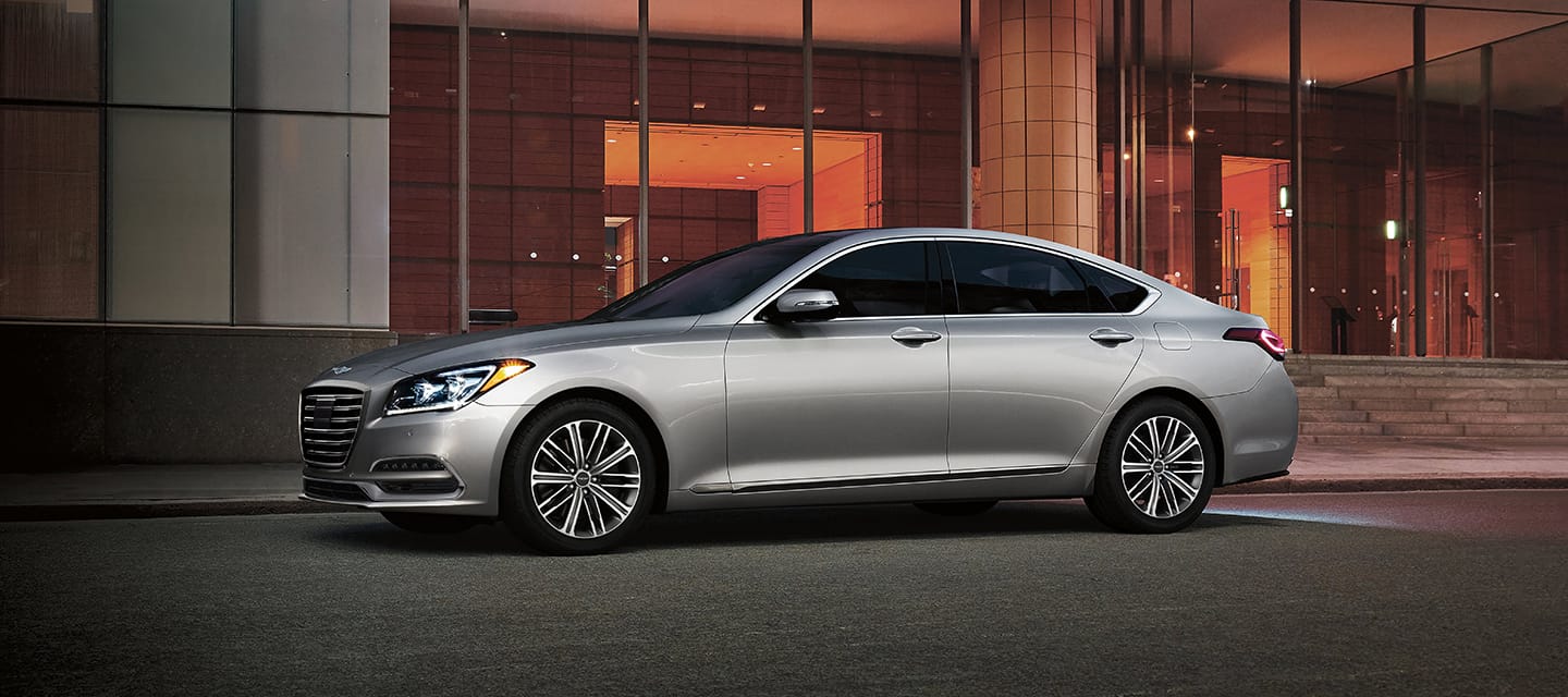 A silver Genesis Car parked outside a modern building at night.