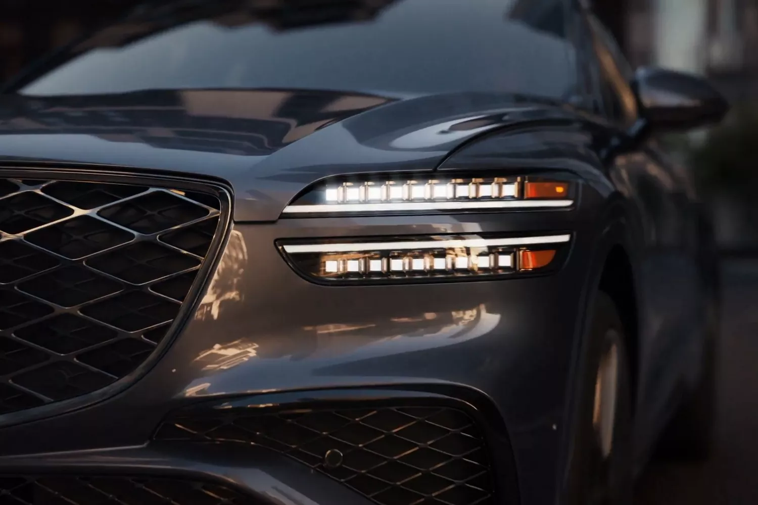 A close-up look at a Genesis GV70 car's front, featuring sleek headlights and a distinctive grille design.