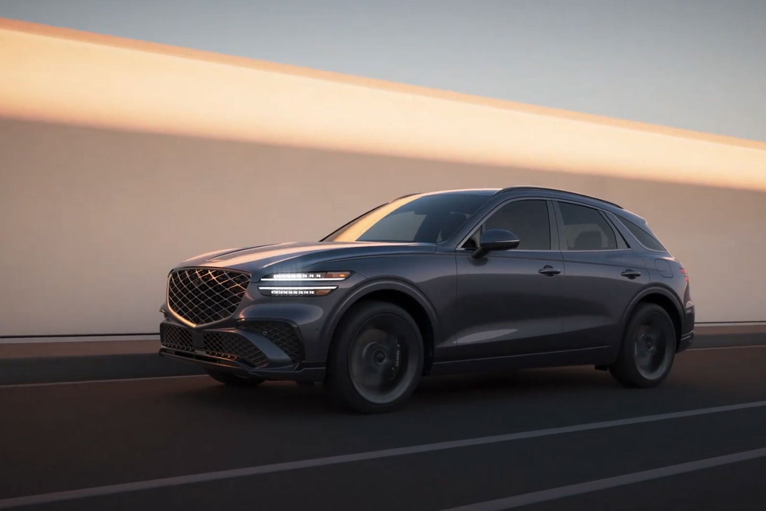 Gray Genesis GV70 SUV driving on a city road at sunset.