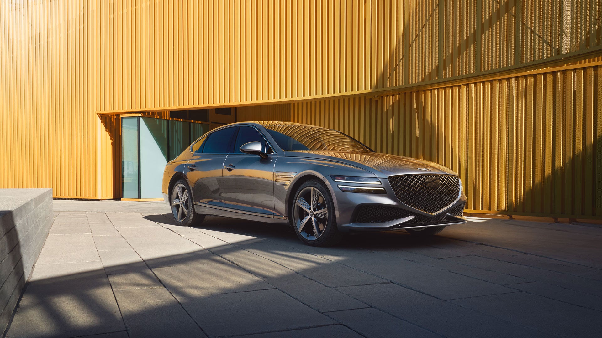 A sleek luxury sedan parked in front of a corrugated wall under bright sunlight.