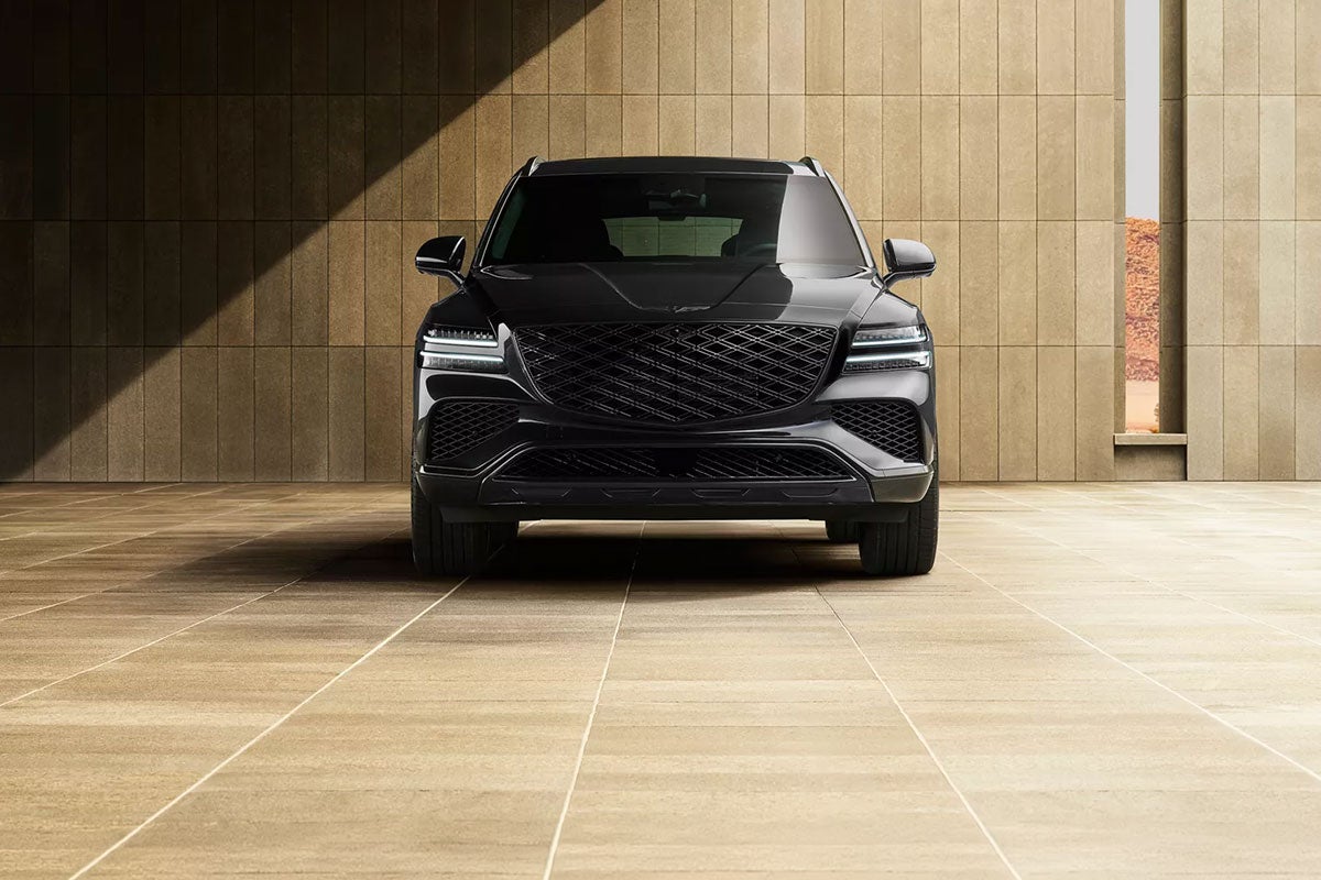 A black Genesis GV80 SUV parked in an empty, modern architectural space with brown tiled walls.