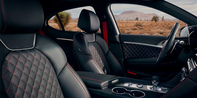 Interior of a Genesis G70 with black leather seats featuring quilted patterns and red stitching, set against a desert landscape.