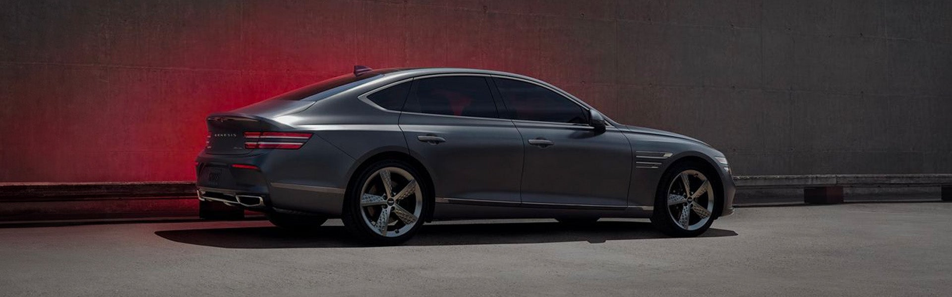 A sleek luxury sedan viewed from the side, parked against a concrete wall under soft lighting.