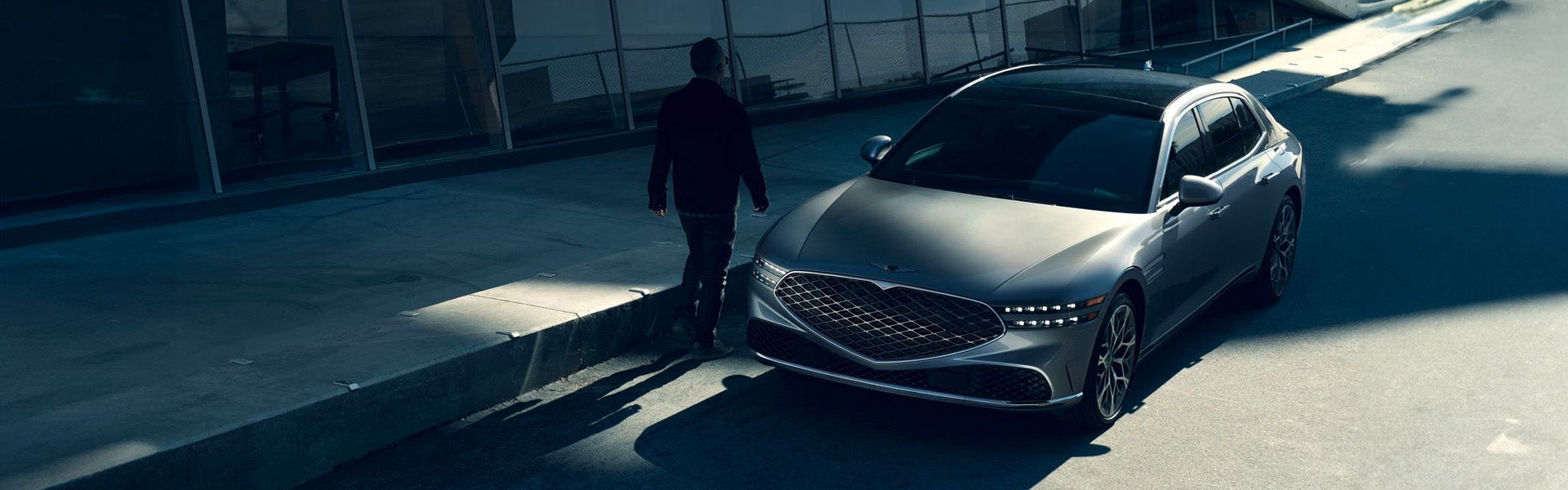 A luxury sedan Genesis G90 with a streamlined design, parked in a shadowy urban setting under soft natural light.