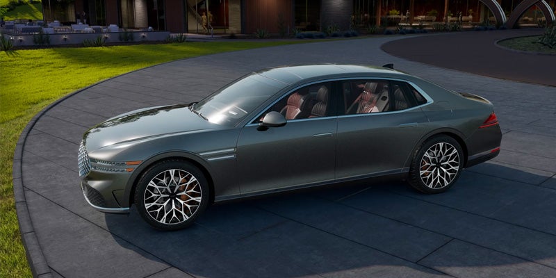 A sleek Genesis luxury sedan shown from the side, parked outdoors with modern architecture in the background.