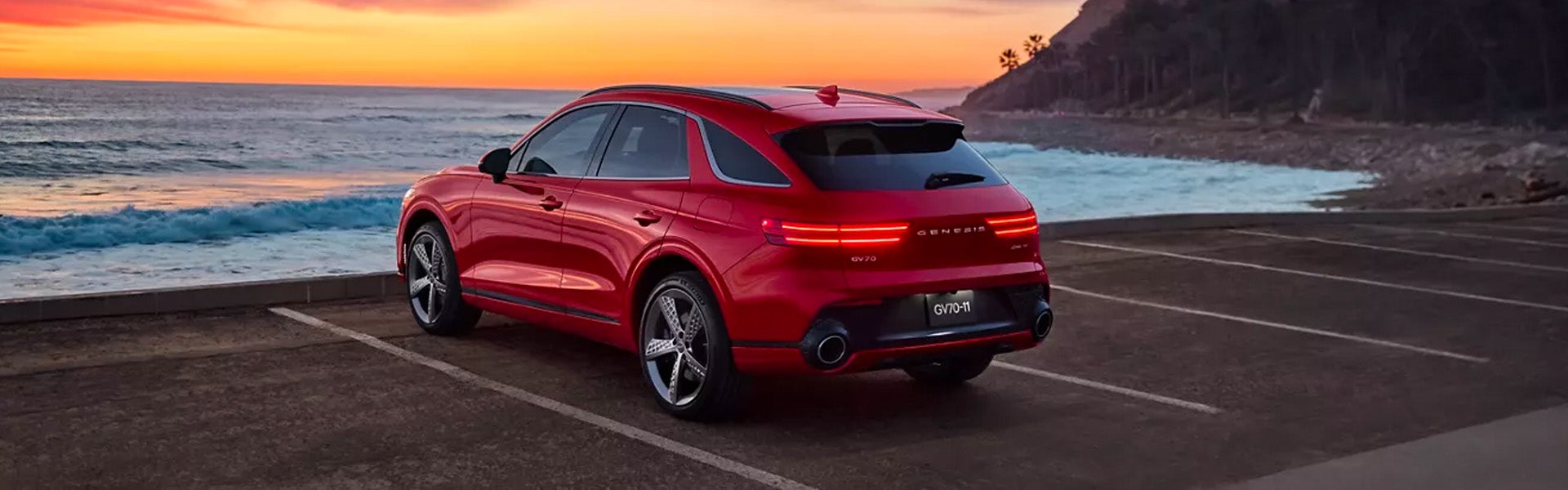 A Genesis GV70 SUV parked by the ocean at sunset.