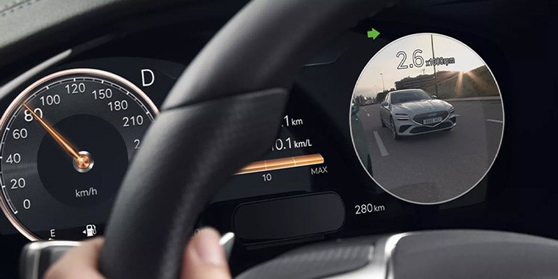 Close-up of a Genesis G70's steering wheel and dashboard display showing speedometer, odometer, and navigation information.