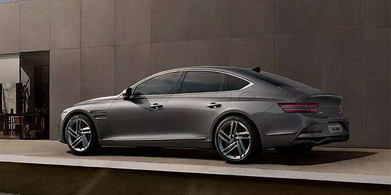 A sleek, silver Genesis G80 sedan parked on a modern stone platform, with a minimalist building in the background.