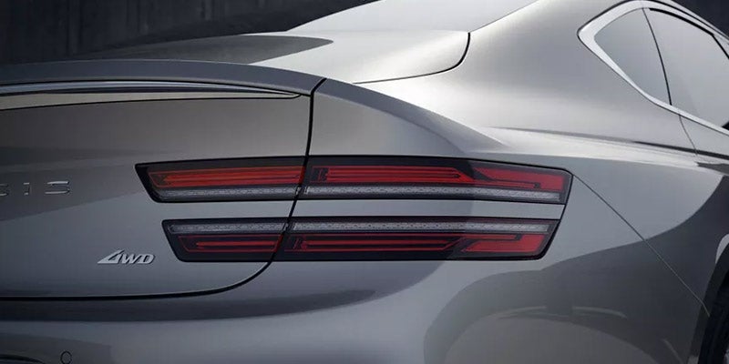 A close-up view of the rear of a gray Genesis G80, highlighting the sleek tail lights and 4WD branding.
