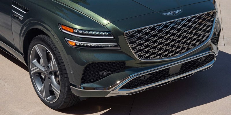 Close-up of the front grille and headlights of a green Genesis GV80 SUV.