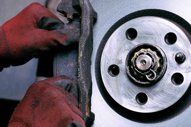 A close-up of a person's gloved hands working on a vehicle brake system, showing the brake caliper and rotor.